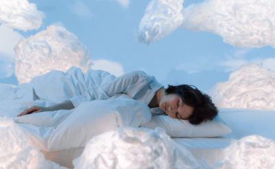 Femme endormie paisiblement sur un lit entouré de nuages doux et blancs, illustrant une nuit de sommeil apaisant et réparateur grâce aux bienfaits du CBD/CBN et de la mélatonine, idéaux pour réduire l'insomnie et les crises d'angoisse.